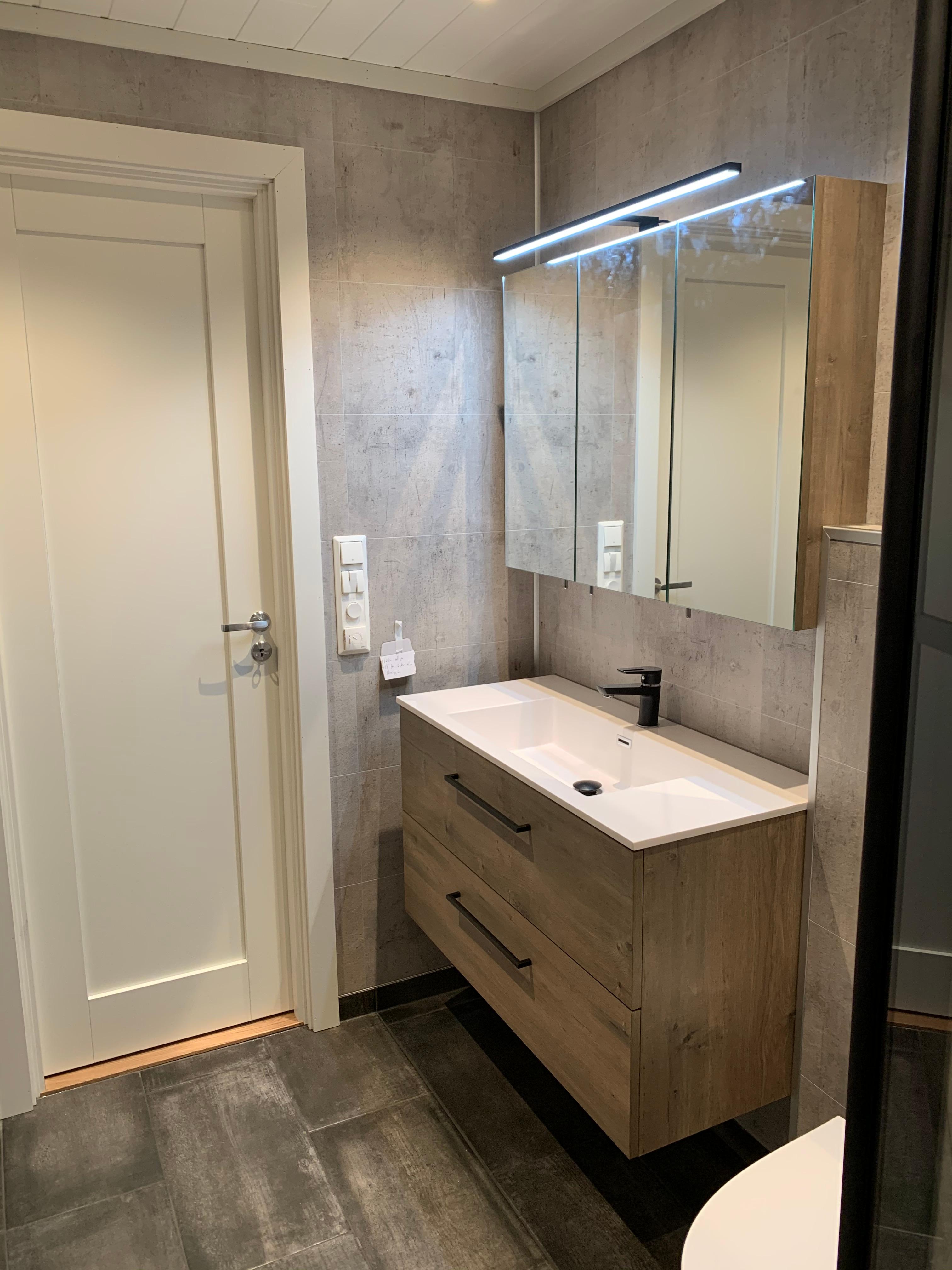 A new bathroom with a wood-toned vanity and a lit mirror