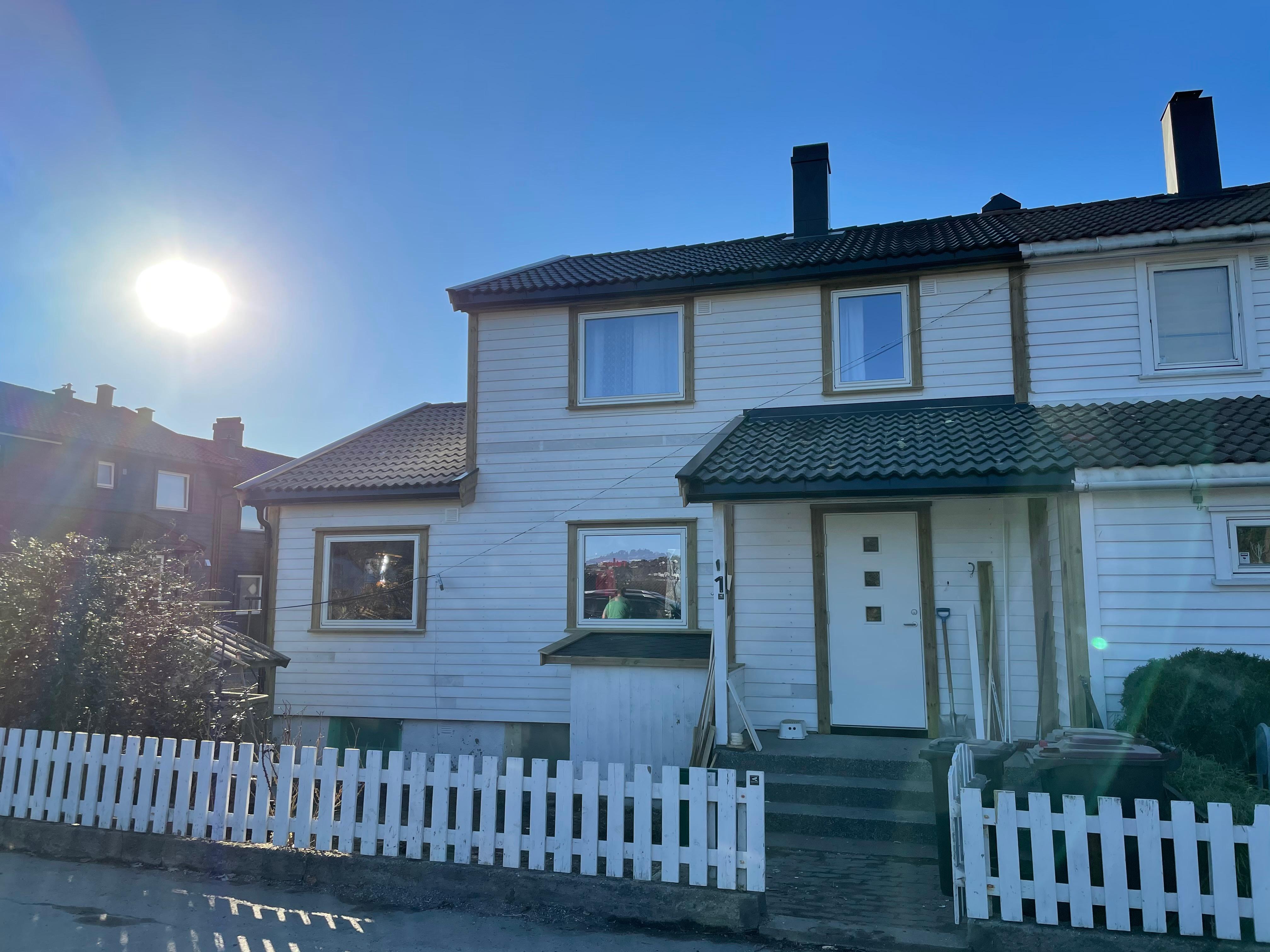 A white two-storey house with a black roof behind a white picket fence