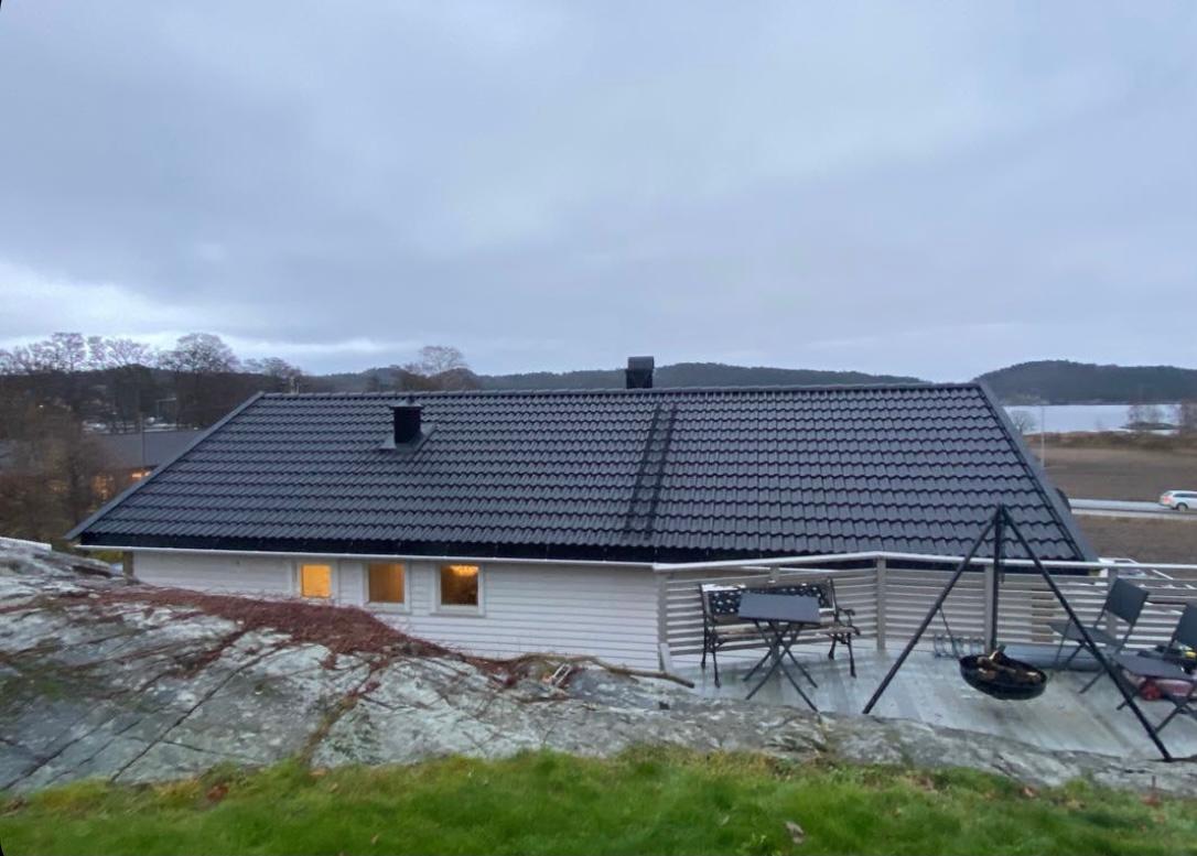 A low house with a dark roof and a terrace, fields behind